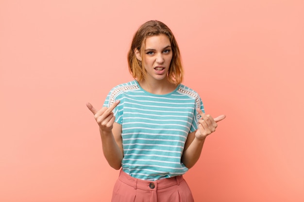 Jeune femme blonde se sentant provocante, agressive et obscène, renversant le majeur, avec une attitude rebelle contre le mur de couleur plat