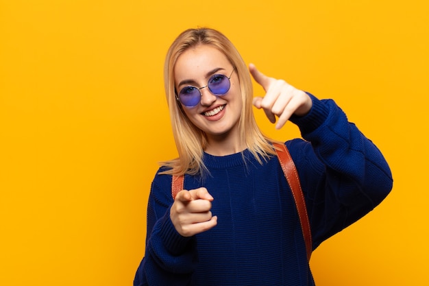 Jeune femme blonde se sentir heureuse et confiante, pointant vers l'avant avec les deux mains et en riant, en vous choisissant