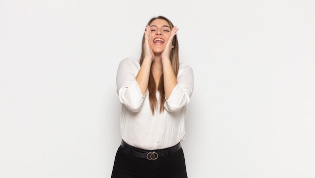 Jeune femme blonde se sentir heureuse, excitée et positive, donnant un grand cri avec les mains à côté de la bouche, appelant