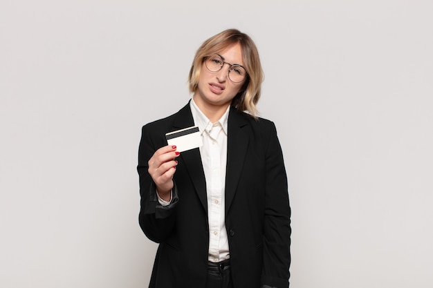 Jeune femme blonde se sentir perplexe et confus, avec une expression stupide et stupéfaite en regardant quelque chose d'inattendu