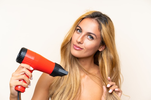 Jeune femme blonde avec sèche-cheveux sur un mur isolé