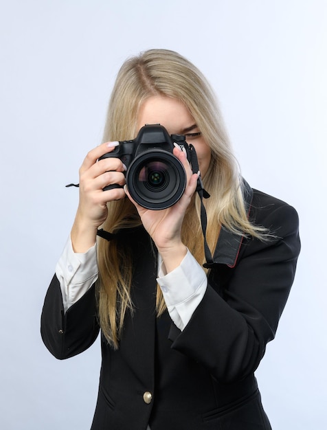 Jeune femme blonde séduisante avec des appareils photo reflex numériques modernes prenant des photos sur fond blanc