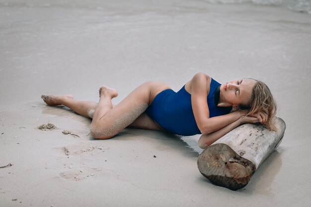 Jeune femme blonde séduisante dans un maillot de bain bleu allongé sur une plage de sable. Concept de vacances d'été