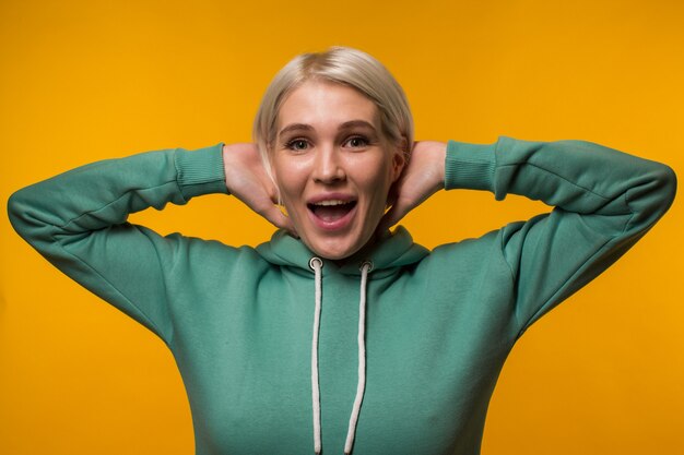 Jeune femme blonde séduisante tandis que le sweat à capuche vert représente l'émotion de surprise