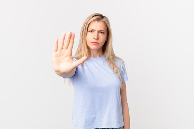 Jeune femme blonde à la sérieuse montrant la paume ouverte faisant un geste d'arrêt