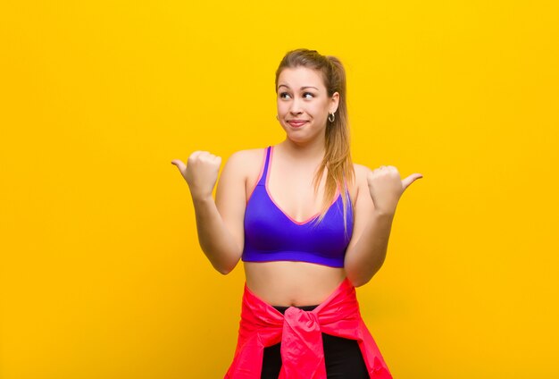 Jeune femme blonde souriant joyeusement et l'air heureux, se sentant insouciant et positif avec les deux pouces vers le haut