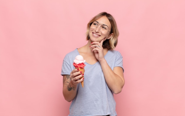 Jeune femme blonde souriant joyeusement et rêvassant ou doutant, regardant sur le côté