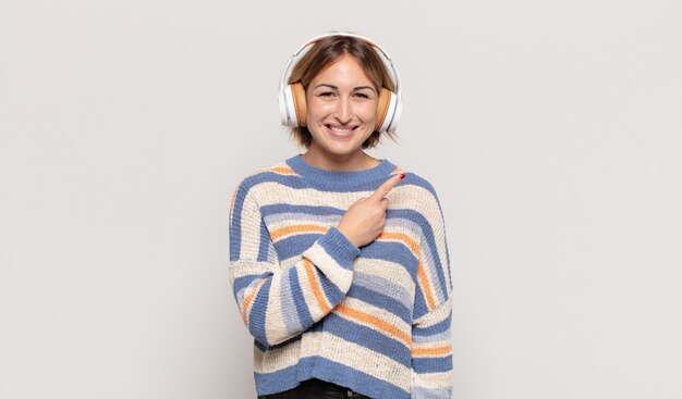 Jeune femme blonde souriant joyeusement, se sentant heureux et pointant vers le côté et vers le haut, montrant l'objet dans l'espace de copie