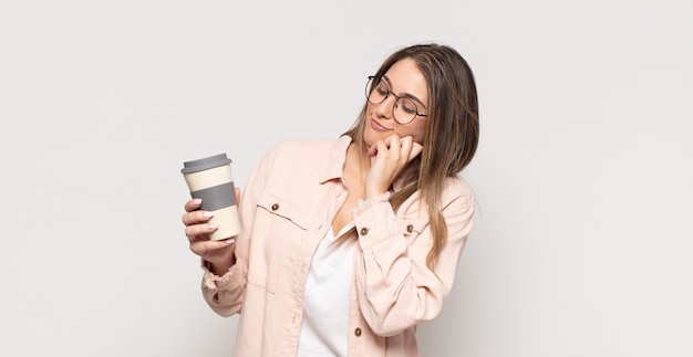 Jeune femme blonde souriante avec une expression heureuse et confiante avec la main sur le menton, se demandant et regardant sur le côté