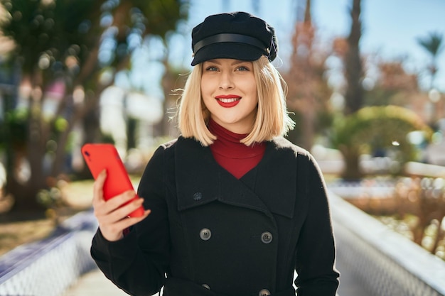 Jeune femme blonde souriante heureuse à l'aide de smartphone au parc