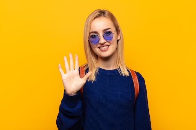 Jeune femme blonde souriante et semblant amicale, montrant le numéro cinq ou cinquième avec la main vers l'avant, compte à rebours