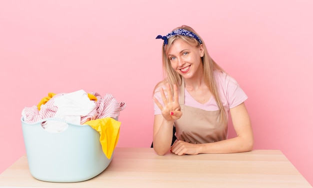 Jeune femme blonde souriante et semblant amicale, montrant le numéro quatre. laver les vêtements concept