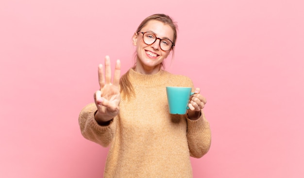 Jeune femme blonde souriante et semblant amicale, montrant le numéro trois ou troisième avec la main vers l'avant, compte à rebours