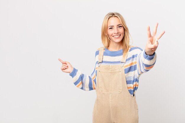 Jeune femme blonde souriante et semblant amicale, montrant le numéro trois