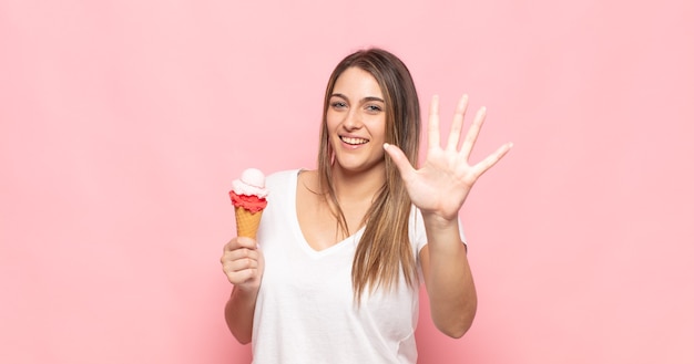 Jeune femme blonde souriante et à la sympathique, montrant le numéro cinq ou cinquième avec la main en avant, compte à rebours