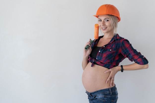 Jeune femme blonde avec un sourire sur son visage regarde le photographe .. Fille enceinte. Tenez le rouleau à peinture. Espace de copie.