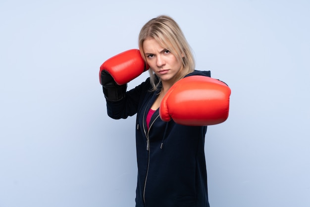 Jeune femme blonde sport sur mur bleu isolé avec des gants de boxe