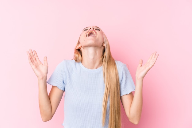 Jeune femme blonde sur une surface rose criant vers le ciel, levant les yeux, frustrée.