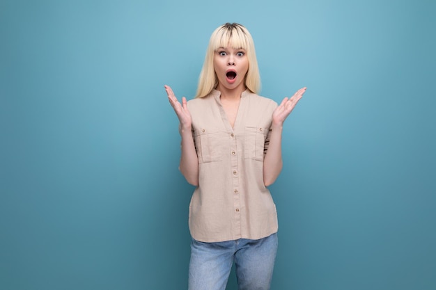 Jeune femme blonde surprise en chemise sur fond bleu studio