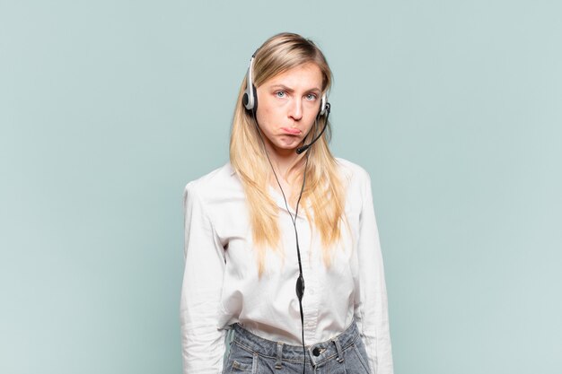 Jeune femme blonde de télévendeur se sentant triste et pleurnicharde avec un regard malheureux, pleurant avec une attitude négative et frustrée