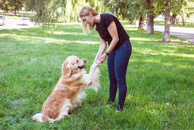 Jeune femme blonde tenant un chien par les pattes avant. Chien de race retriever avec jouer avec une fille dans le parc