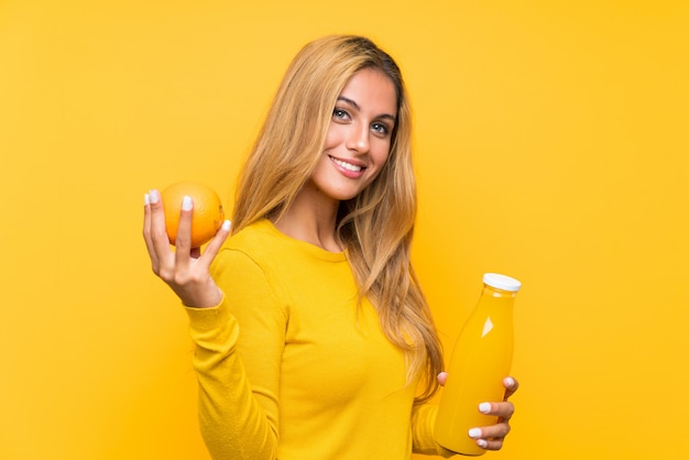 Jeune femme blonde tenant un jus d'orange sur jaune