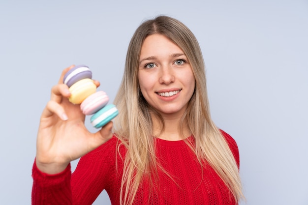 Jeune femme blonde tenant des macarons français colorés et avec une expression heureuse