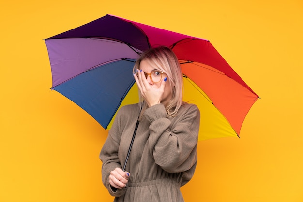 Jeune femme blonde tenant un parapluie couvrant les yeux et regardant à travers les doigts