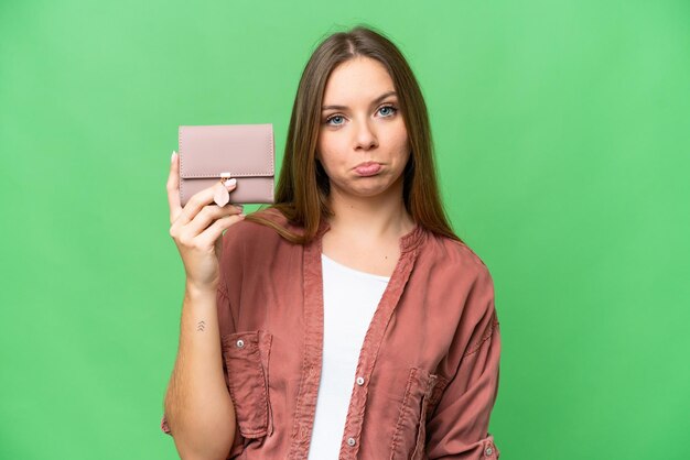 Jeune femme blonde tenant un portefeuille sur fond isolé chroma key avec une expression triste