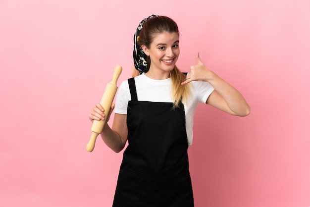 Jeune femme blonde tenant un rouleau à pâtisserie isolé sur un mur rose faisant un geste de téléphone. Rappelez-moi signe