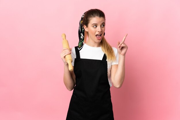 Photo jeune femme blonde tenant un rouleau à pâtisserie isolé sur un mur rose pensant une idée pointant le doigt vers le haut