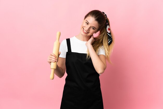 Jeune femme blonde tenant un rouleau à pâtisserie isolé en riant