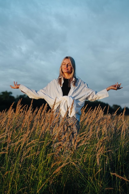 Jeune femme blonde en train de méditer, regardant au loin debout au milieu d'un champ de blé