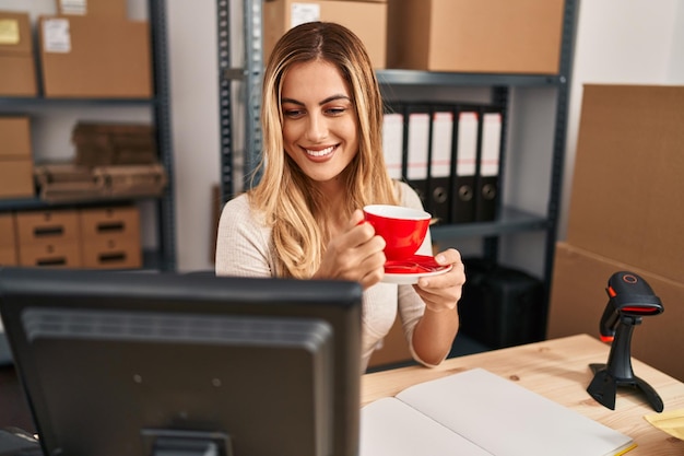 Jeune femme blonde travaillant dans une entreprise de commerce électronique, buvant du café au bureau