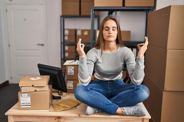 Jeune femme blonde travaillant dans une entreprise de commerce électronique faisant du yoga assis sur une table au bureau