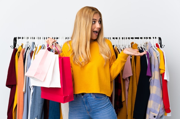 Jeune femme blonde uruguayenne dans un magasin de vêtements et tenant des sacs à provisions avec une expression faciale surprise