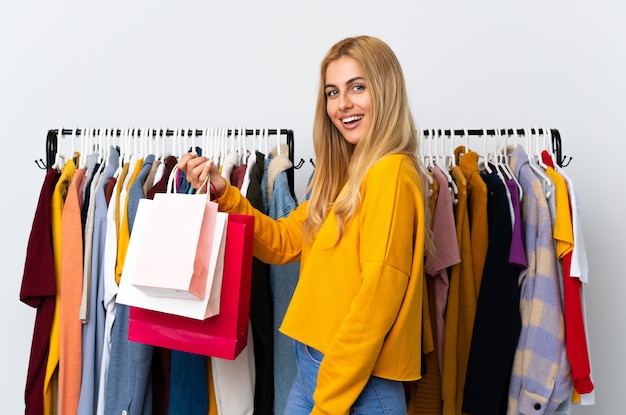 Jeune femme blonde uruguayenne dans un magasin de vêtements et tenant des sacs à provisions souriant beaucoup