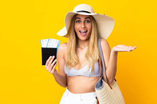 Jeune femme blonde uruguayenne en maillot de bain tenant un passeport sur fond jaune isolé avec une expression faciale choquée