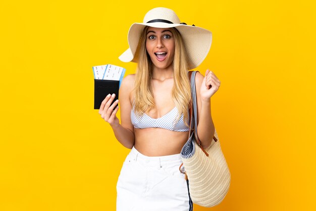 Jeune femme blonde uruguayenne en maillot de bain tenant un passeport sur fond jaune isolé avec une expression faciale surprise et choquée
