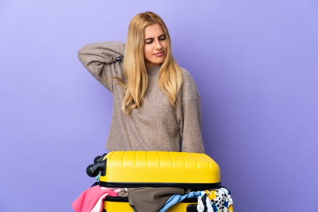 Jeune femme blonde uruguayenne avec une valise pleine de vêtements sur un mur violet isolé avec des maux de cou