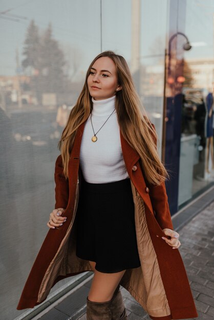 Jeune femme blonde en vêtements d'automne se promène sur les vitrines de fond de rue