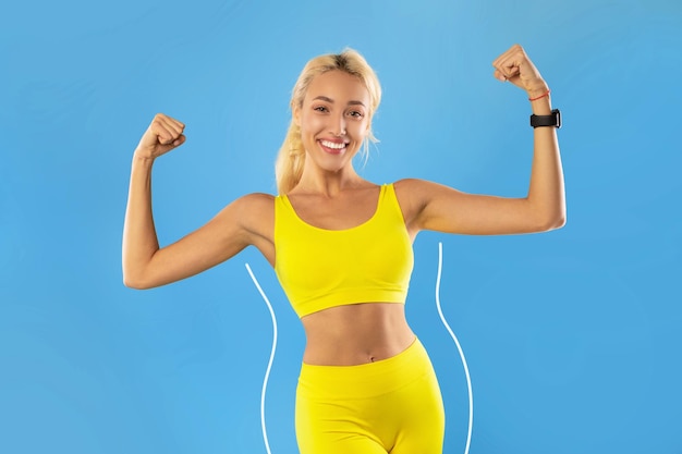 Jeune femme blonde en vêtements de sport montrant les muscles du biceps gardant un régime amincissant faisant du sport pour