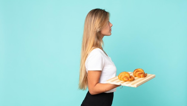 Jeune femme blonde en vue de profil pensant, imaginant ou rêvant et tenant un plateau à croissants