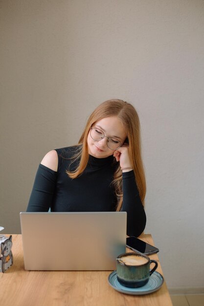 Une jeune femme en blouse noire travaille à la pige dans un café Une étudiante au travail à distance boit du café