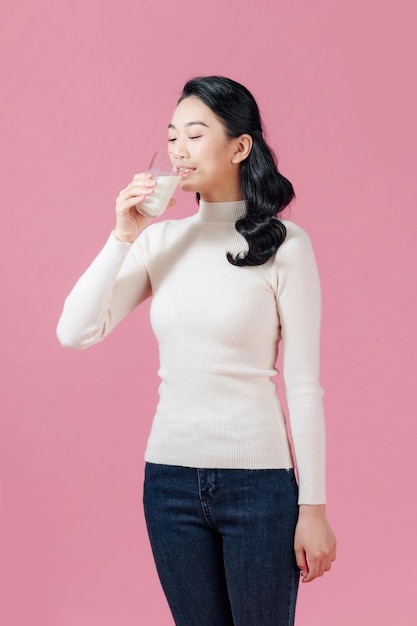 Jeune femme boire un verre de lait femelle sourire heureux isolé sur fond rose concept organique naturel