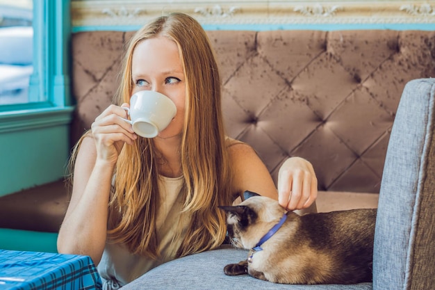 La jeune femme boit du café et caresse le chat Dans le contexte du canapé rayé par les chats