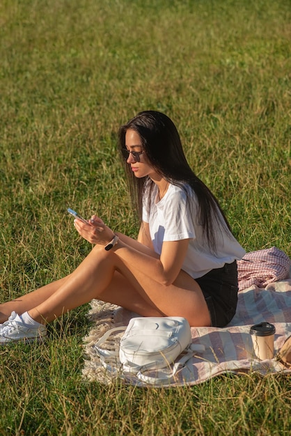 Une jeune femme boit du café et se détend dans le parc sur l'herbe.