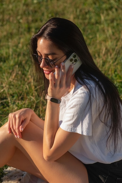 Une jeune femme boit du café et se détend dans le parc sur l'herbe.