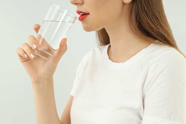 Jeune femme boit de l'eau du verre sur fond clair