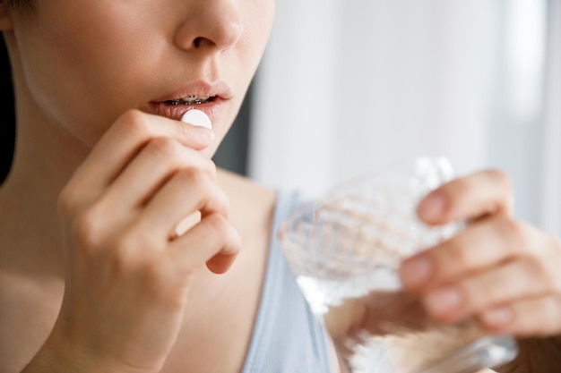 Une jeune femme boit des médicaments et tient un verre d'eau